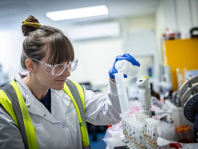 Female analytical chemist pouring substance into container at laboratory