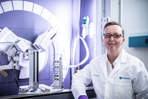 Element scientist in a white coat next to testing equipment in a pharmaceutical testing lab.
