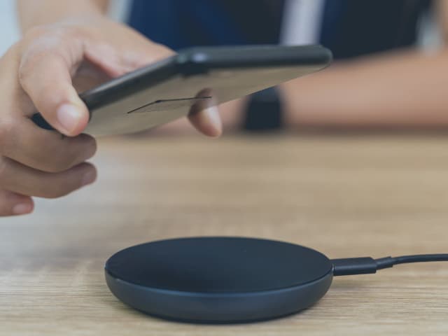 Hand placing a smartphone onto a wireless charging pad for Qi certification testing