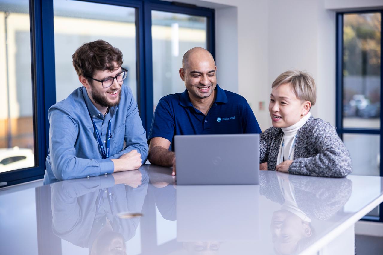 Two customers sitting with an Element testing expert in front of a laptop discussing what they can see on the laptop screen