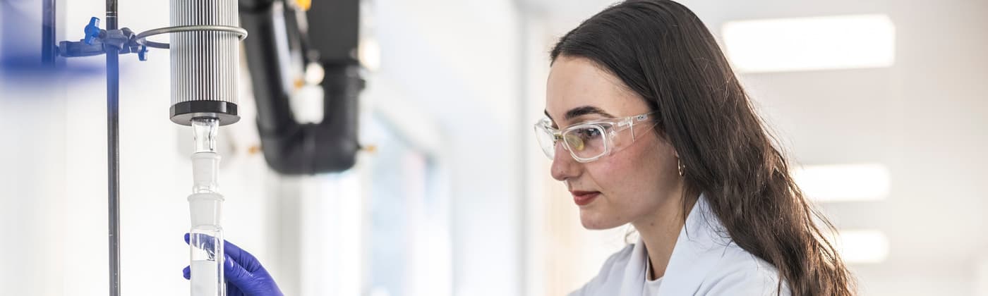 Element scientist in white coat and safety goggles in life sciences testing laboratory interacting with advanced analytical equipment for pharmaceutical research