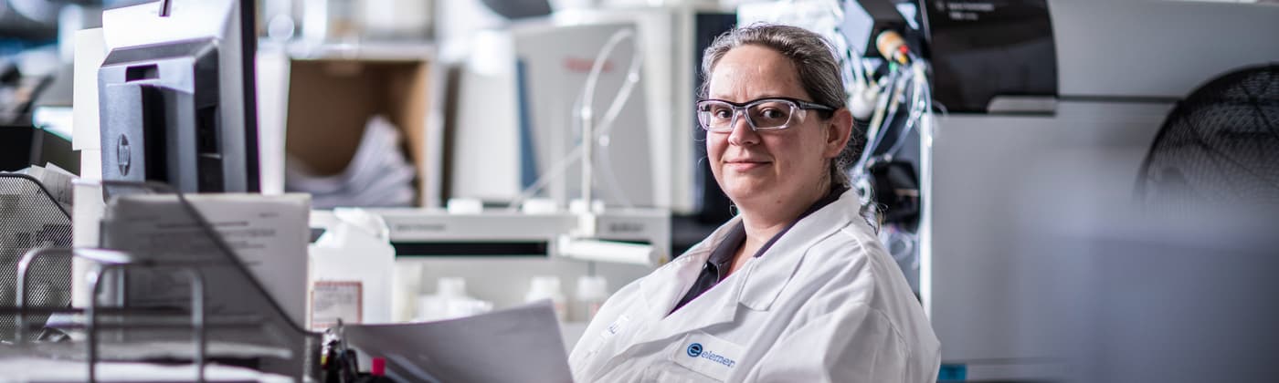 Lab analyst reviewing cosmetic sample data next to elemental analysis instrumentation