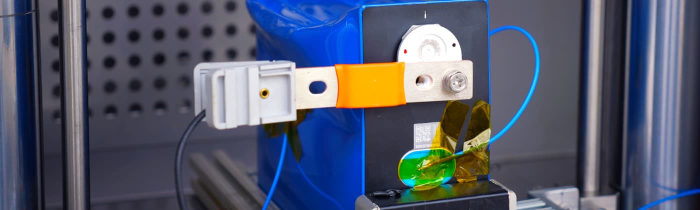 A pouch battery cell undergoing mechanical crush testing in a battery safety screening rig.