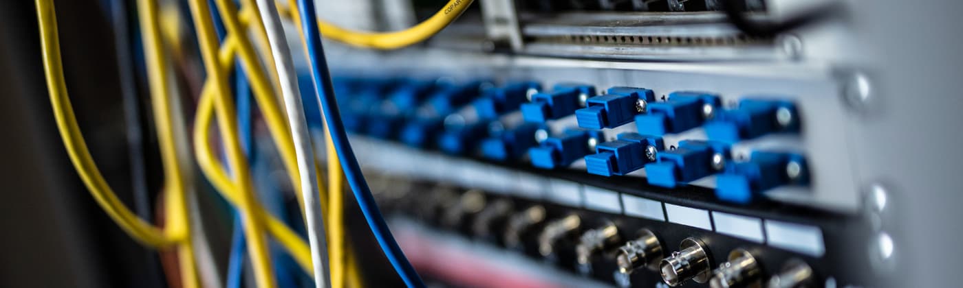 Rack-mounted network equipment with fibre optic cables and blue SC connectors in a telecommunications facility.