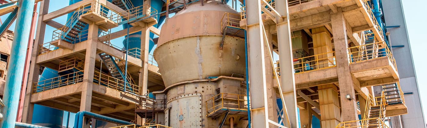 Industrial cement plant with heavy machinery, piping systems, and hazardous area equipment in a manufacturing environment.