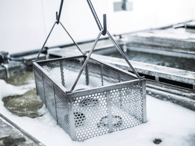 Metal samples in a basket being lowered into a tank