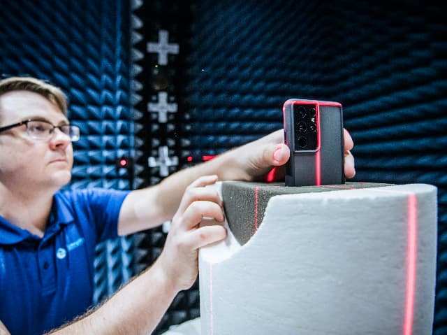 Engineer positioning a smartphone on a test fixture inside an anechoic chamber for PTCRB certification testing