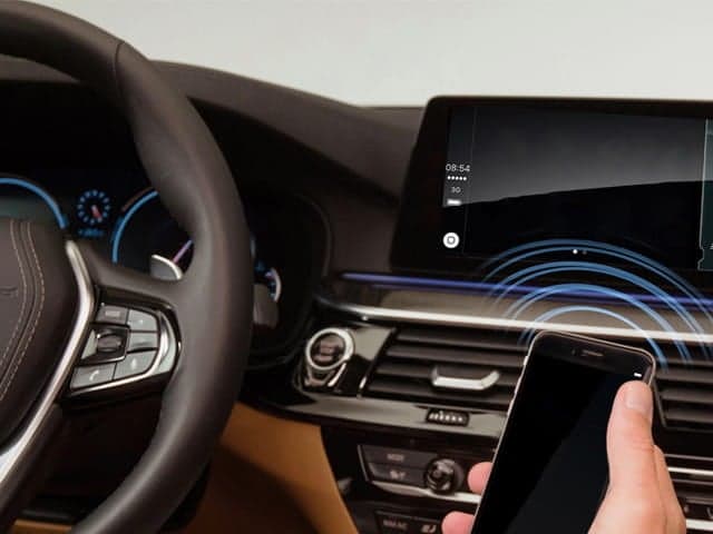 Hand holding phone up to steering wheel in car with visual overlay of bluetooth signals