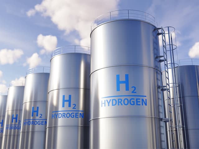 Large industrial hydrogen fuel storage tanks with H2 labelling against a blue sky
