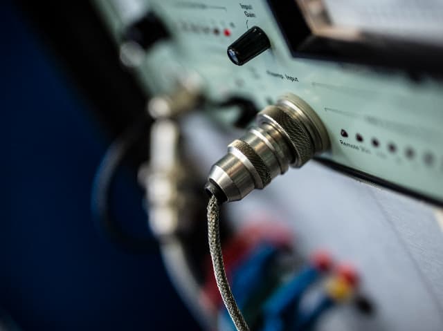 A braided cable connected to a metal connector on electronic test equipment used for audio video safety testing