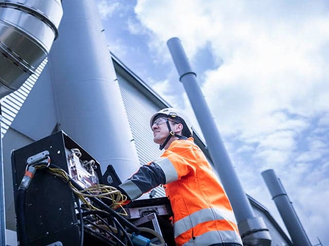 Technician conducting stack emissions testing at industrial facility with cooling towers