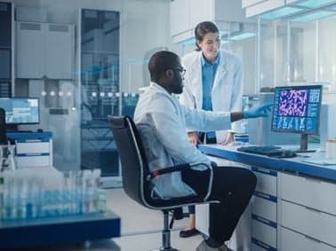 image of two scientists one of whom is sitting down at a compter terminal discussing the data on screen