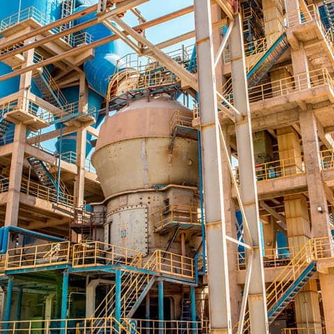 Industrial cement plant with heavy machinery, piping systems, and hazardous area equipment in a manufacturing environment.