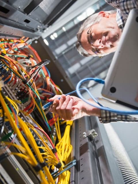 Technician working with electrical wiring in control panel in workshop